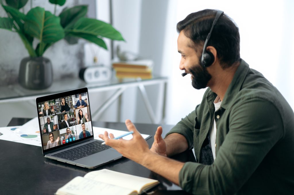 Successful busy mixed race successful man, sitting at work desk in modern office, using laptop talking to multiracial business team via video conference. Virtual online meeting, remote negotiations