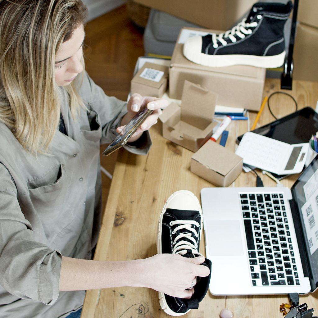 A seller photographing a product for a listing next to a laptop and shipping boxes