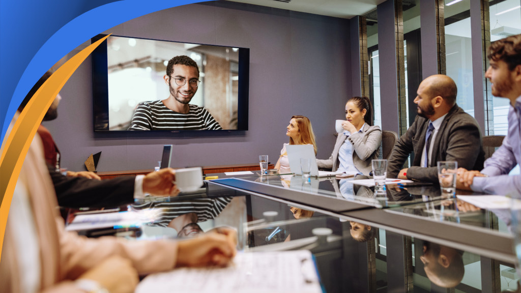 Sales team in a conference room meeting with a remote colleague on a video screen