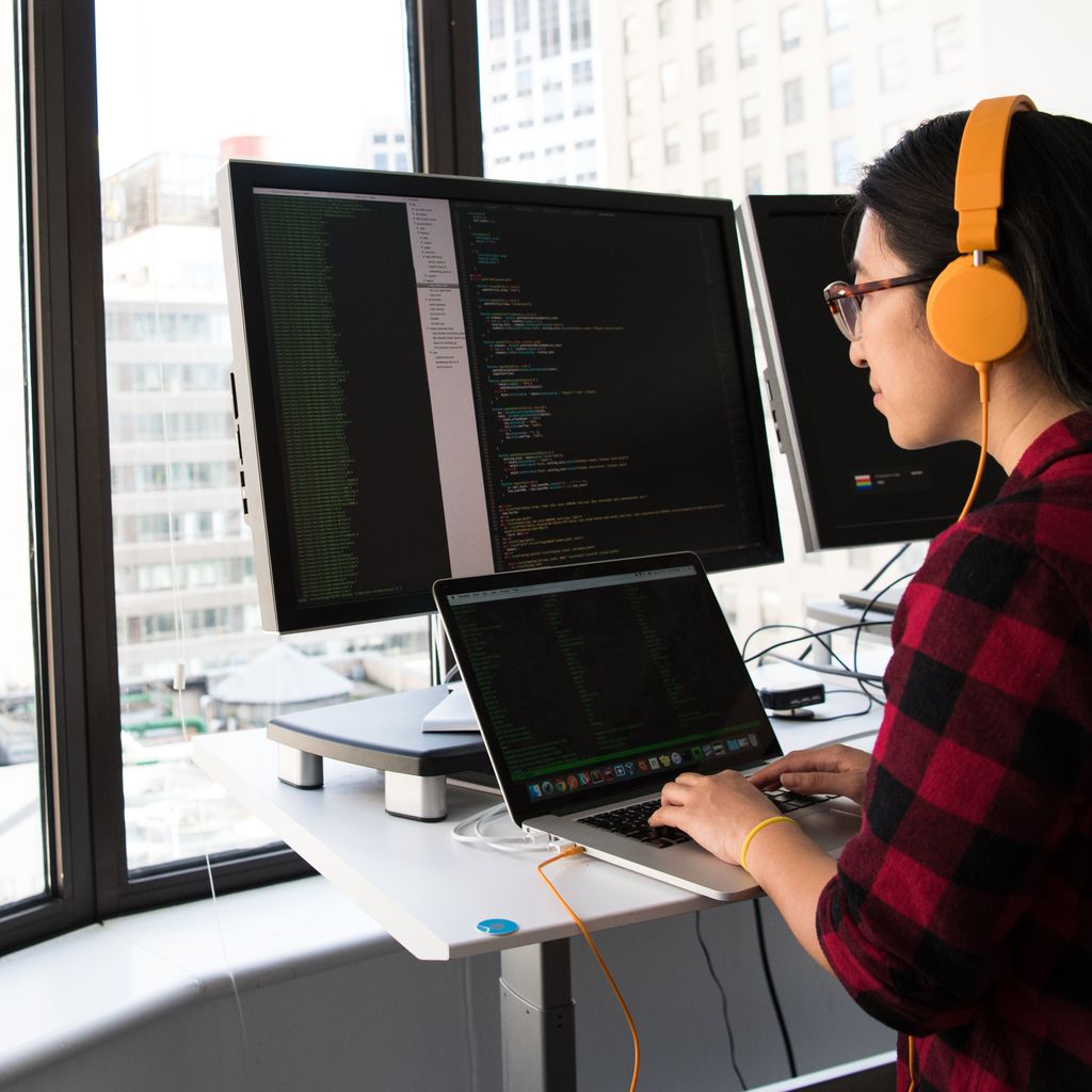 An engineer working at a standing desk with several screens