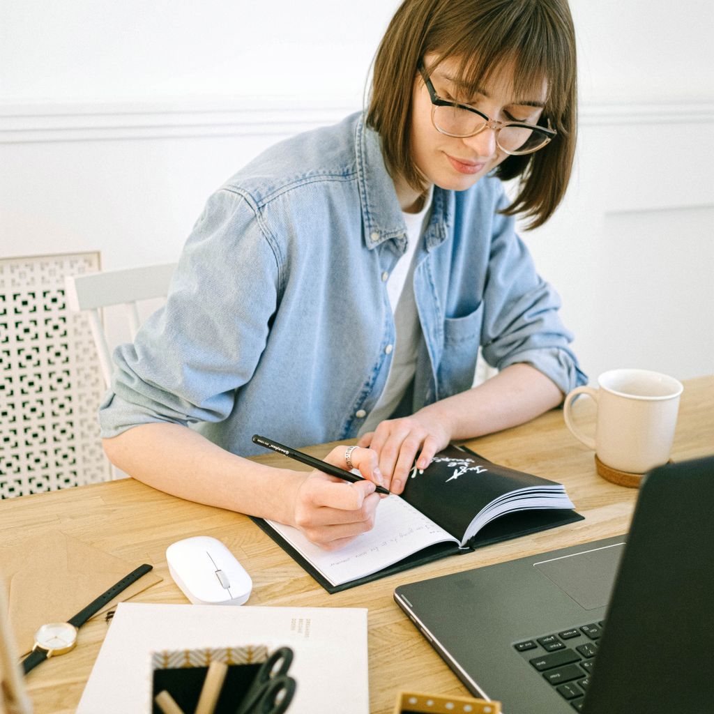 A content marketer drafting notes at her desk next to a laptop