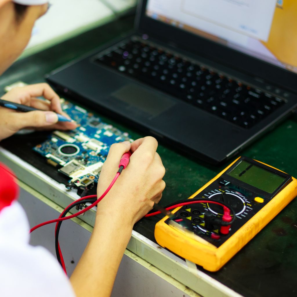 An engineer testing a circuit board next to a laptop