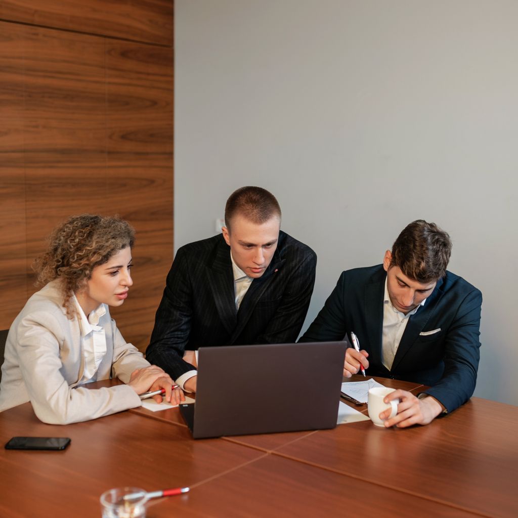Three colleagues working together on a laptop at a meeting table