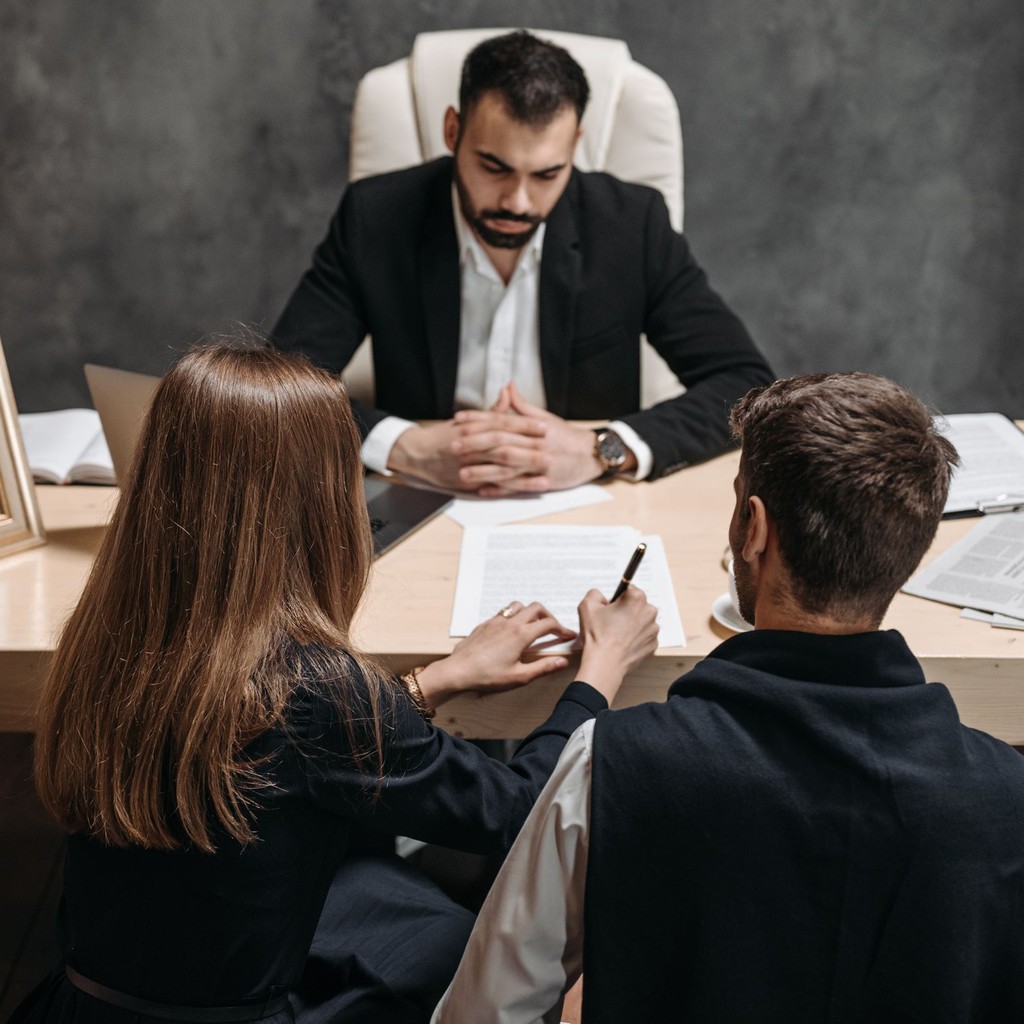 Lawyer meeting two clients across a desk while they sign case paperwork