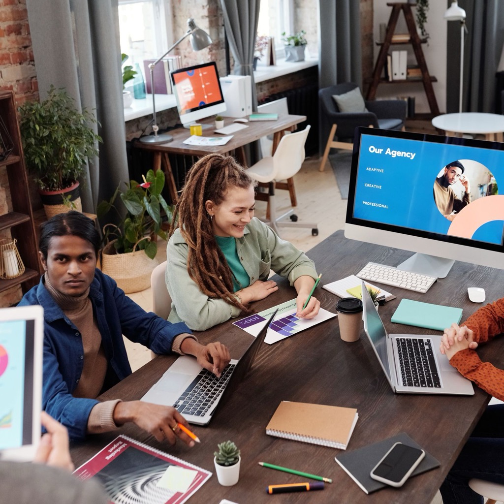 Agency team reviewing client work around a table with laptops and a presentation on screen