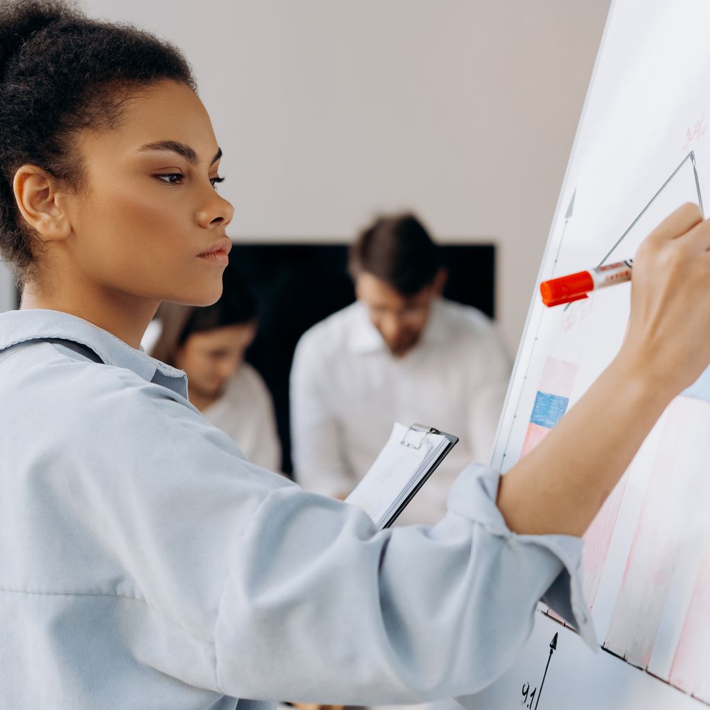An operations manager with a clipboard charting team performance on a whiteboard